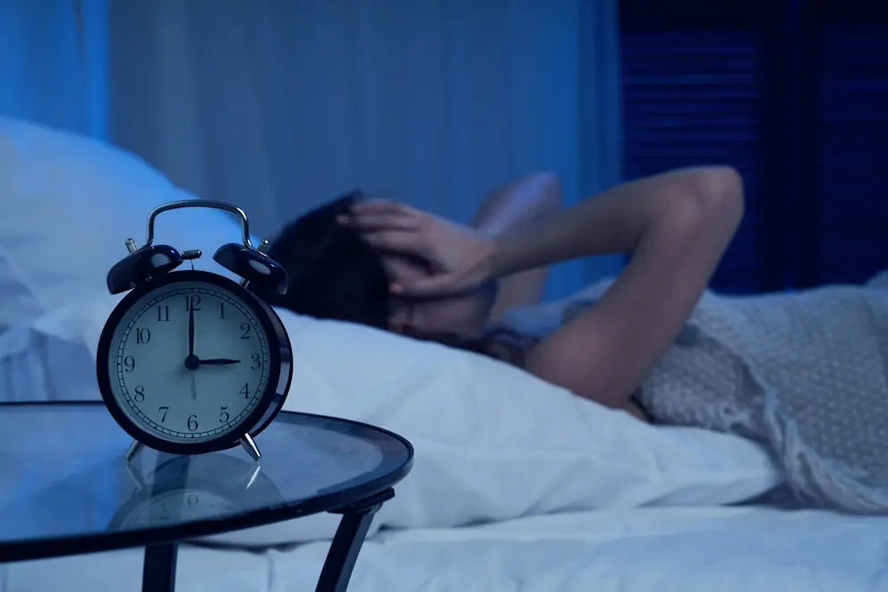 A woman lying awake in bed in the early hours, an alarm clock on the bedside table.