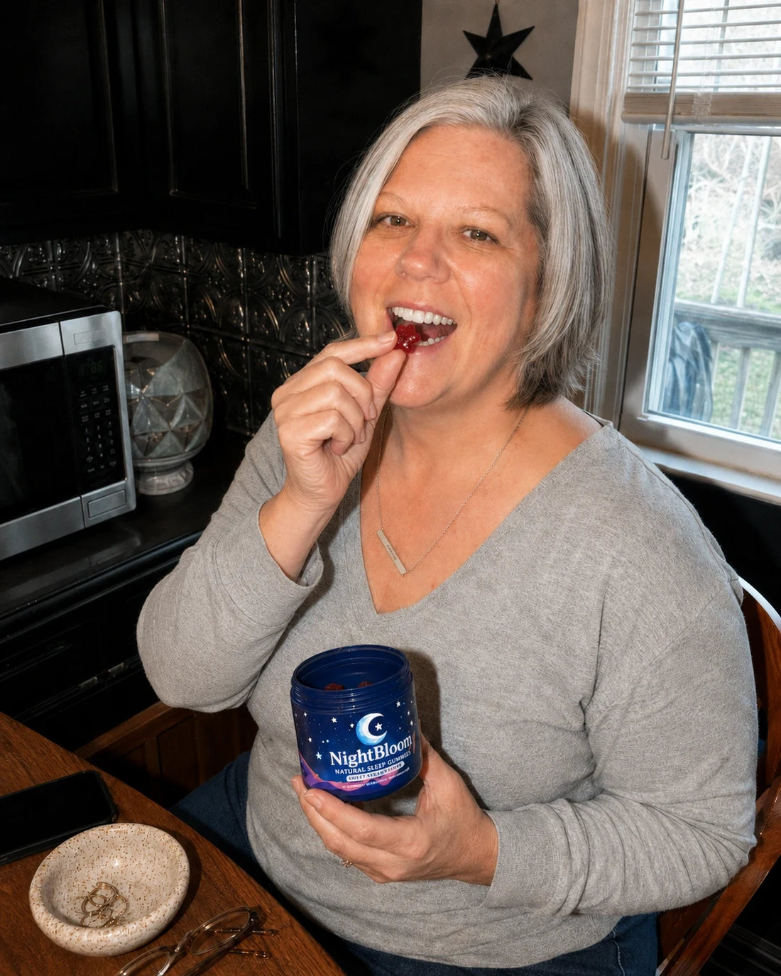 A woman in her kitchen at night enjoying a NightBloom strawberry sleep gummy
