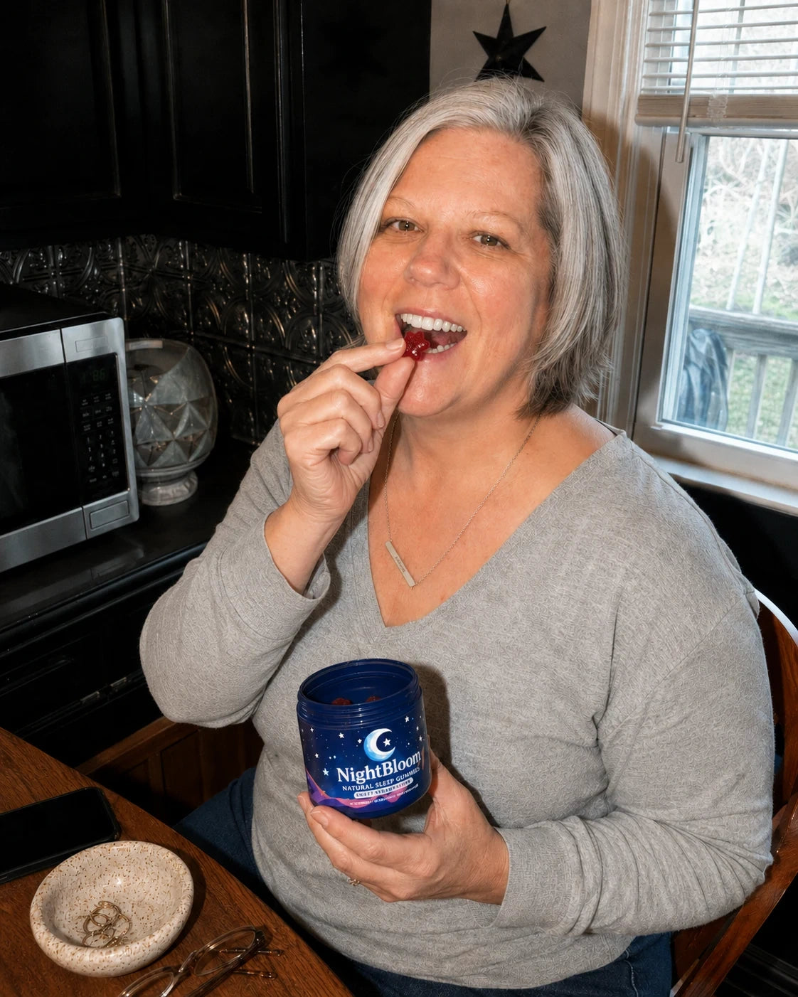 A woman in her kitchen at night enjoying a NightBloom strawberry sleep gummy