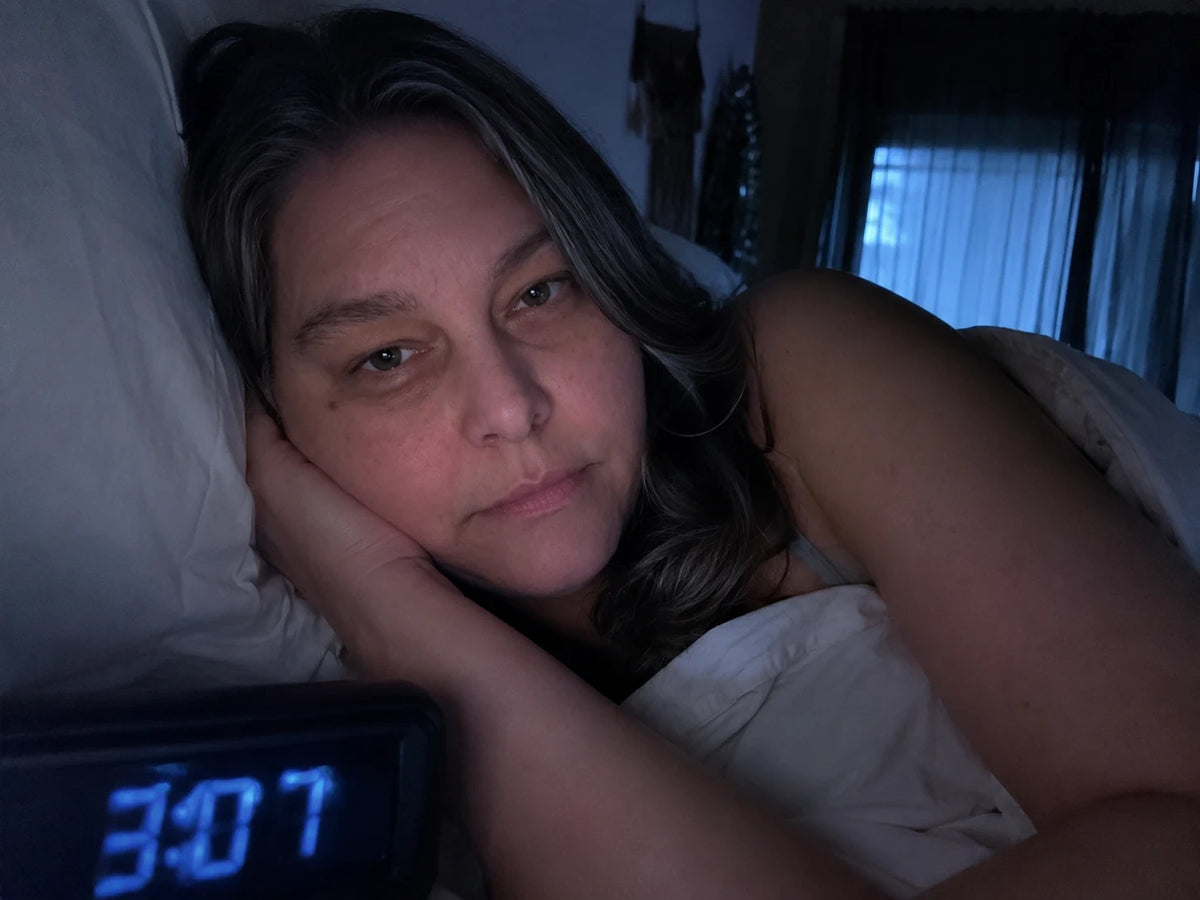 A woman lying awake at night beside a clock reading 3:07 A.M.